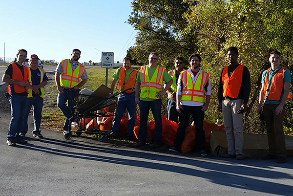 Nine men in fluorescent vests stand in front of Clark lane with orange trash bags 