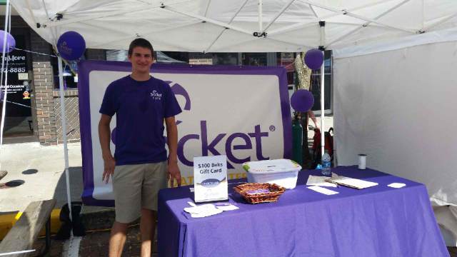 Socketeer Nick Bruemmer stands behind a socket booth on a street in Fulton