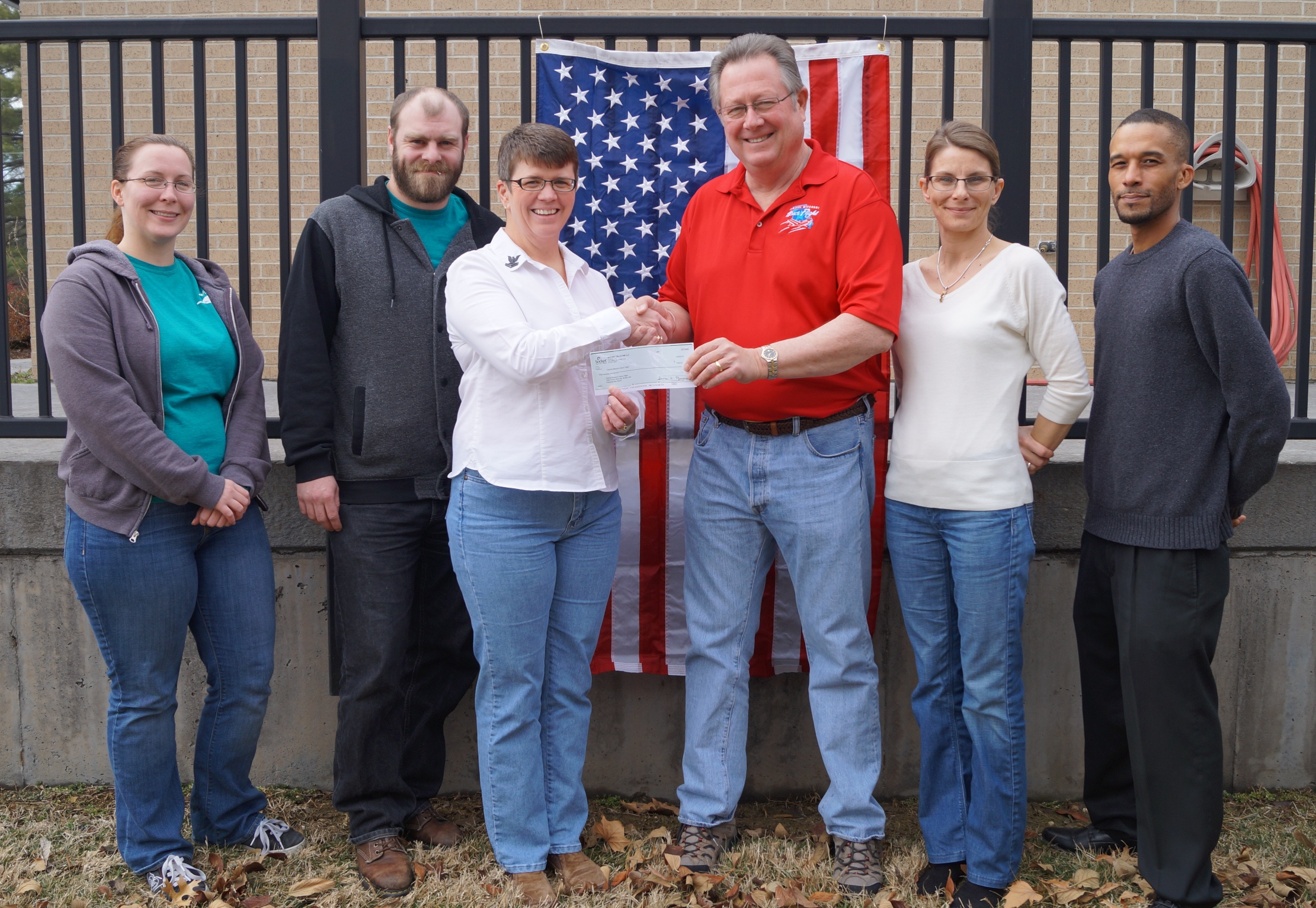 Vicki Winton from socket presents a check to Steve Paulsell from the Central Missouri Honor Flight in from of an American Flag