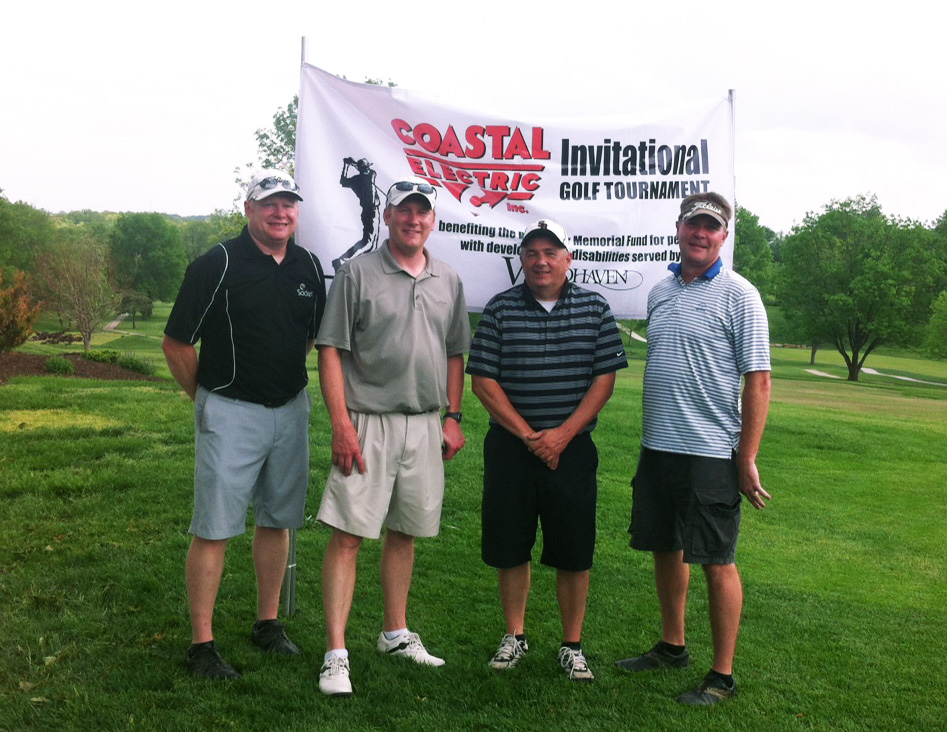 four men stand on a golf course